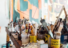 tabletop filled with paintbrushes standing upright in containers