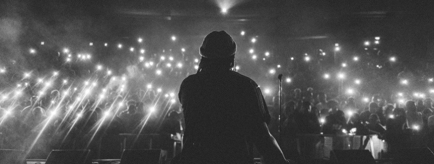 black and white image of the back of a person on a stage performing for an audience