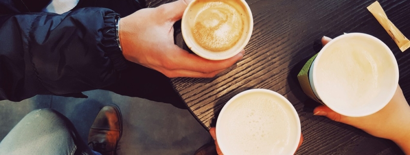 three people sitting around a table drinking coffee.