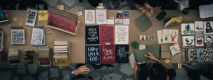 upper view of a table filled with home-made books and surrounded by people making them and looking at them