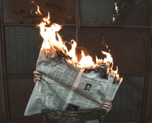 person holding an open newspaper - the top of the paper is on fire