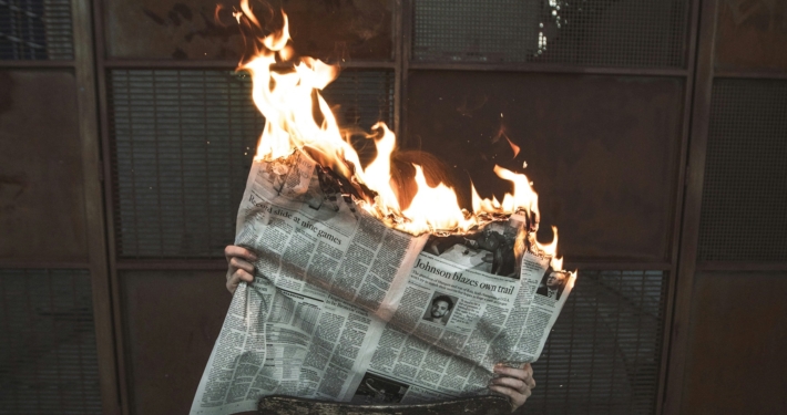 person holding an open newspaper - the top of the paper is on fire