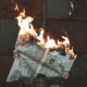 person holding an open newspaper - the top of the paper is on fire