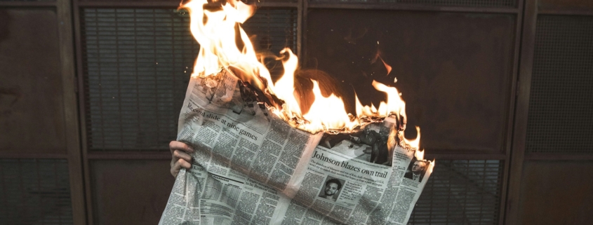 person holding an open newspaper - the top of the paper is on fire